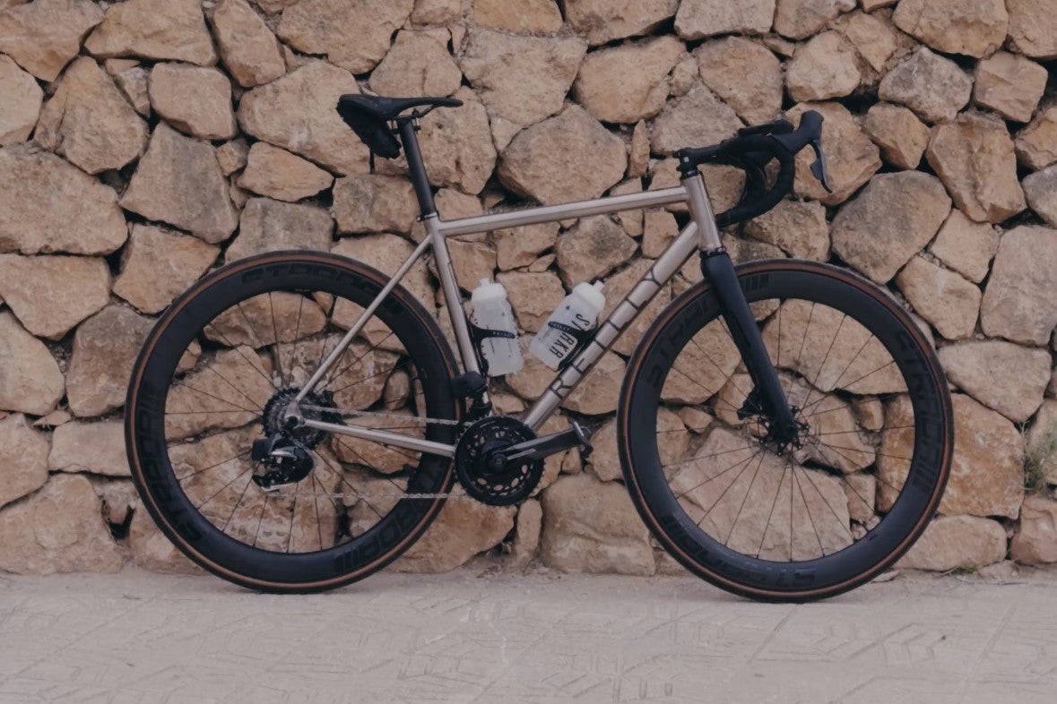 Titanium road bike against a wall of large bricks.