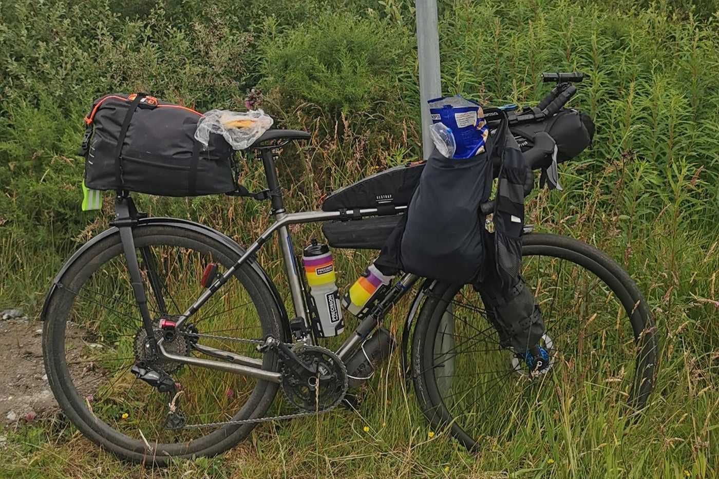 A titanium gravel bike ladened with bags in a field.