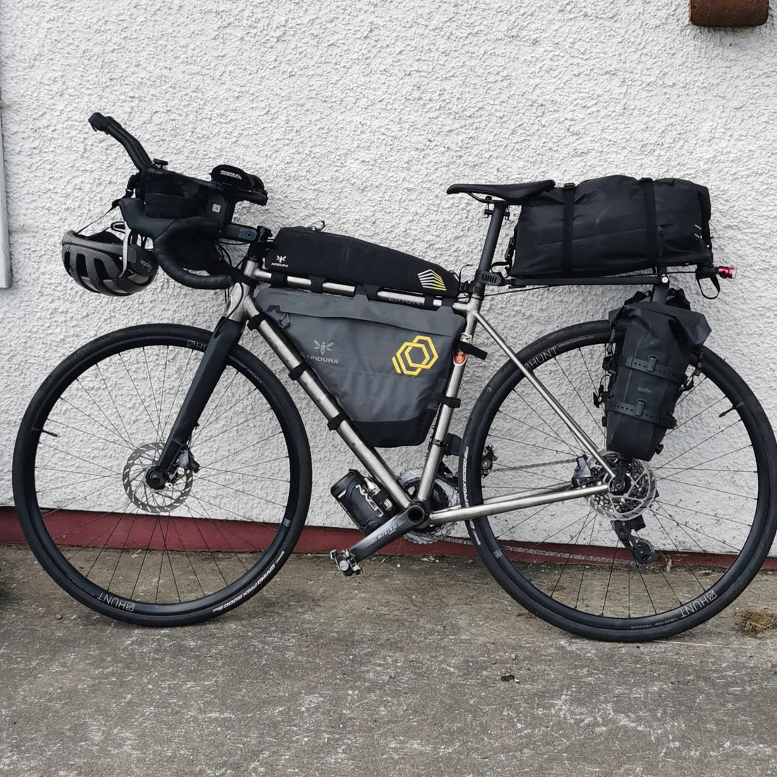 A bike with many bike packing bags leans against a white wall. 