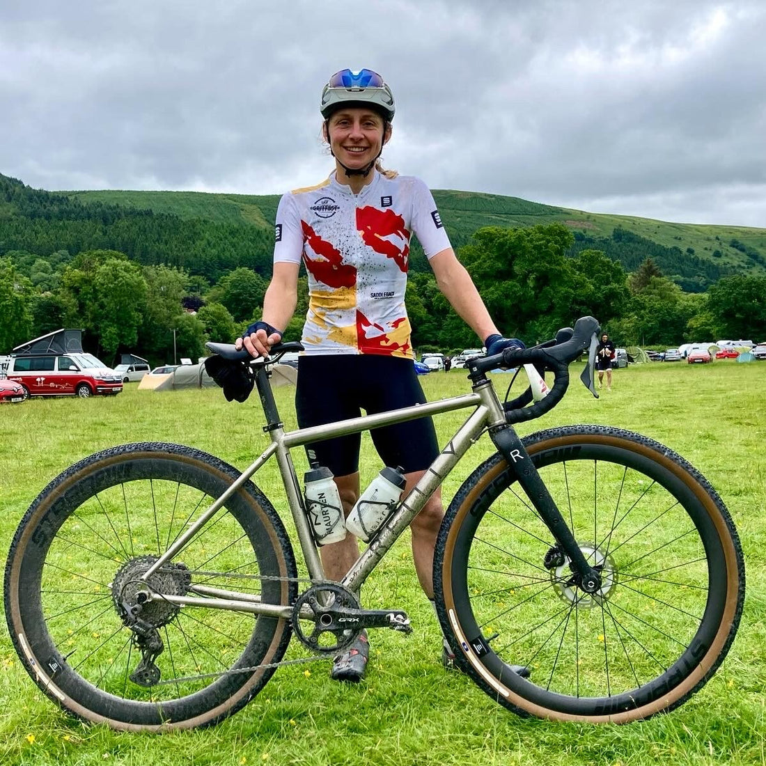 Female cyclist stands behind her titanium bike in a field 