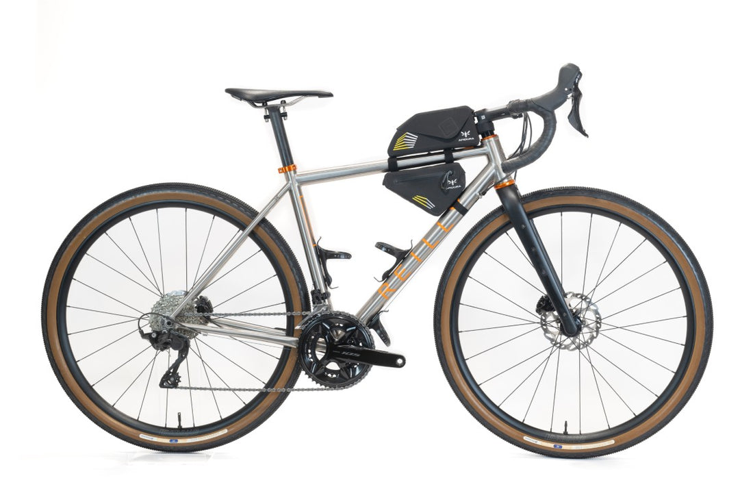 A titanium gravel bike on white with two small apidura bags.