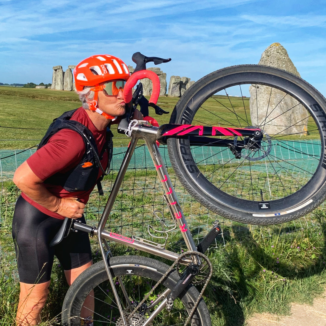 Woman kisses her titanium bicycle with Stonehenge in the background.