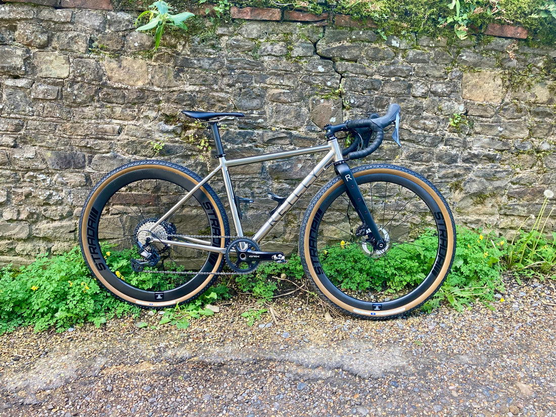 A titanium Reilly bike leaning against a brick wall. 