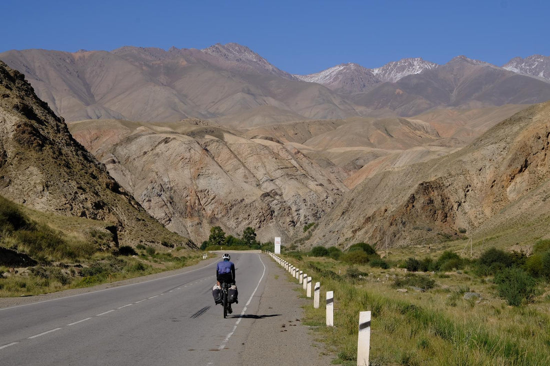 Man with a well packed bike cycles towards mountains 