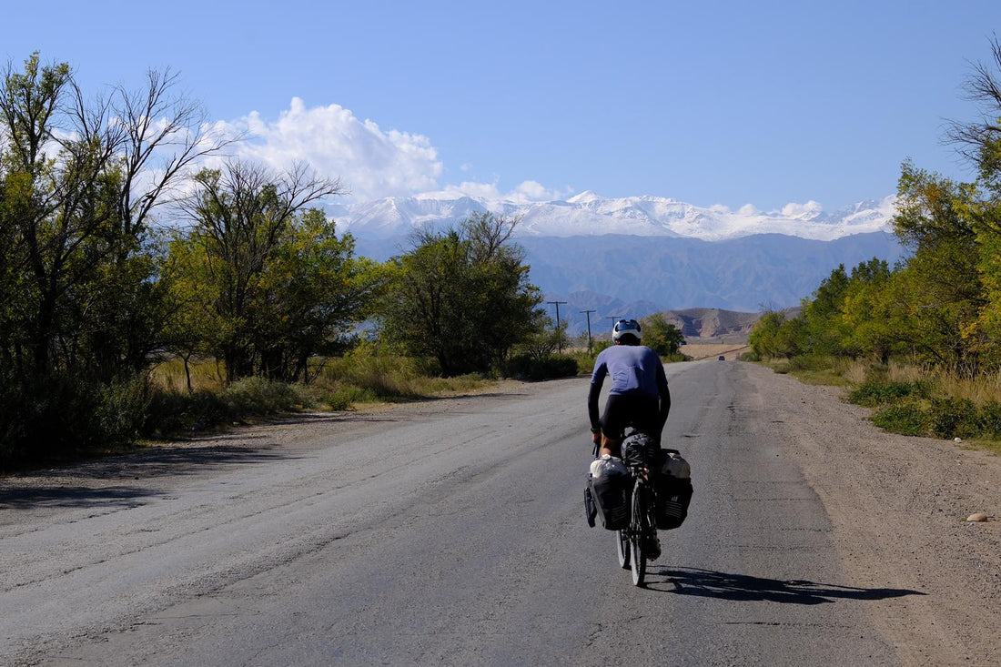 Man with a well packed bike cycles on an empty road with mountains in the distance.