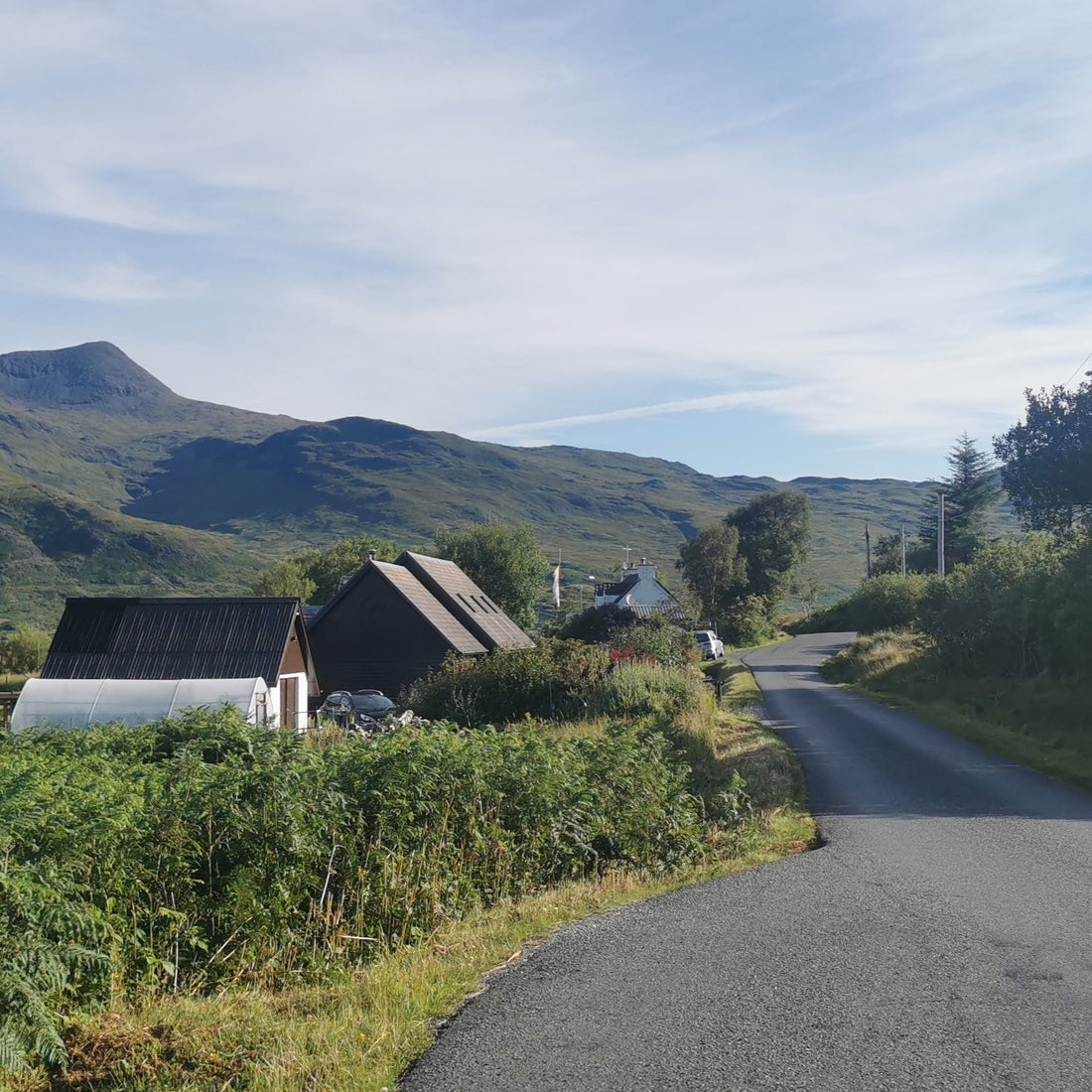 tarmac road with mountains in the far ground and a cottage on the side of the road.