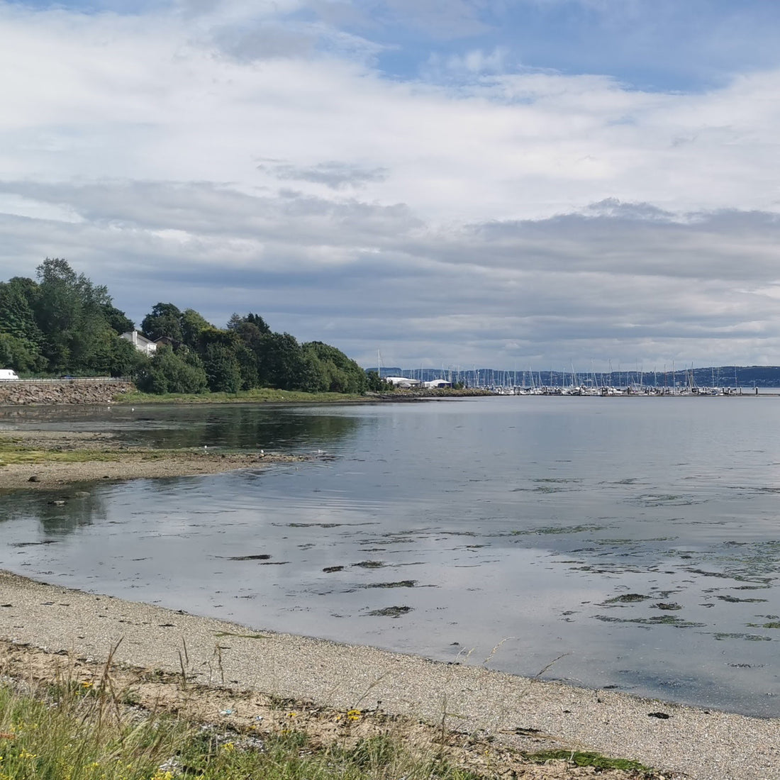 A pebble shoreline with a marina in the far background.