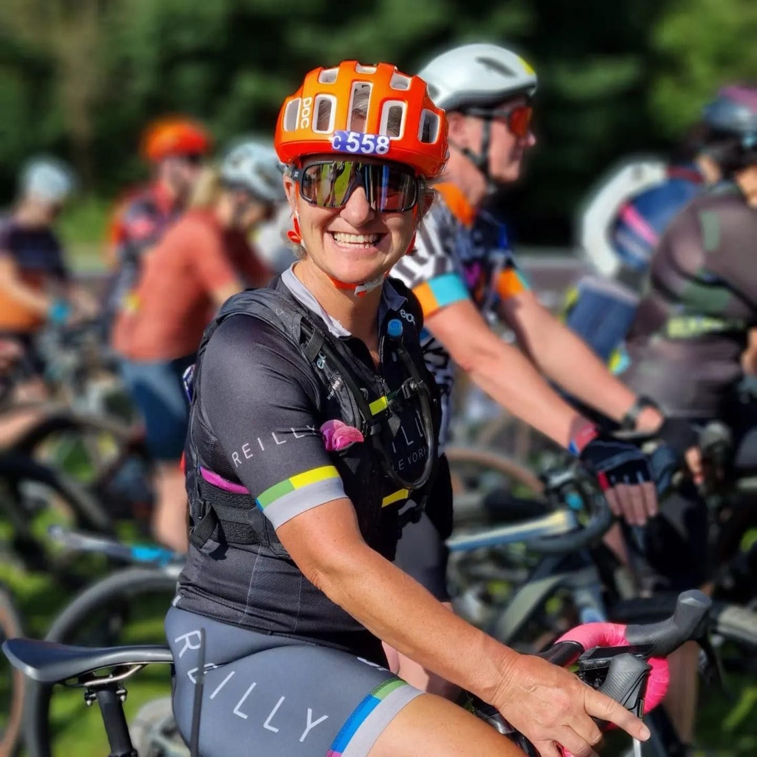 Female cyclist in orange POC helmet smiles at the camera.