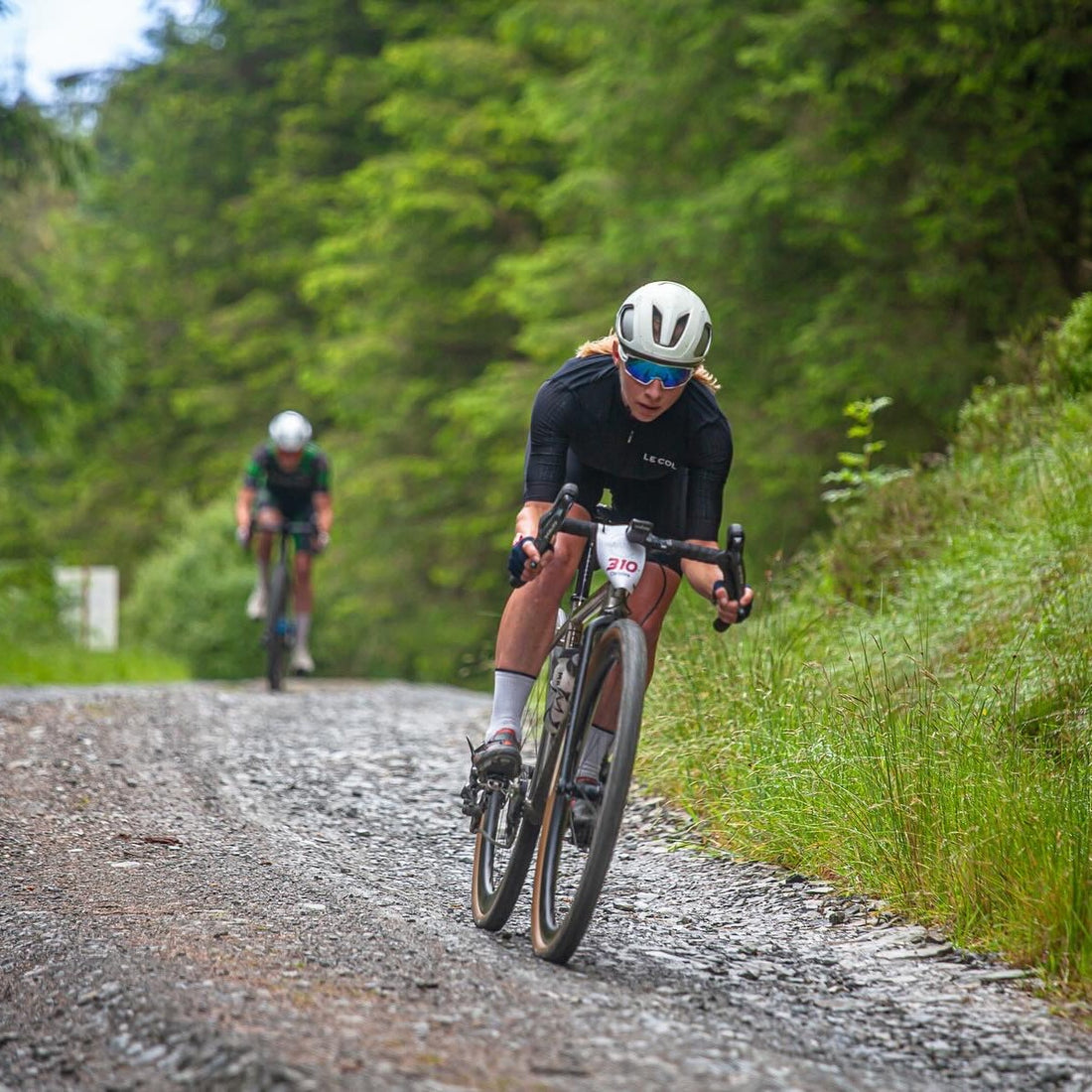 Female cyclist in black top and white helmet cycles fast along a gravel track