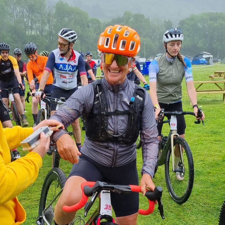 Smiling female cyclist in orange helmet has her race tag checked .