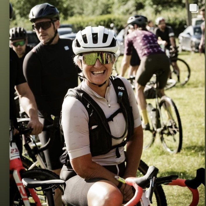 Female cyclist in white helmet and mirror sunglasses smiles at the camera while sitting on her bike 